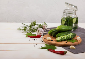 Fermented cucumbers in a glass jar, cucumbers lie on a wooden board, hot red pepper, garlic, dill, gray napkin on a white background. Horizontally.