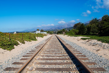 Fototapeta premium Railroad tracks converging in perpective into the distance towards distant mountains