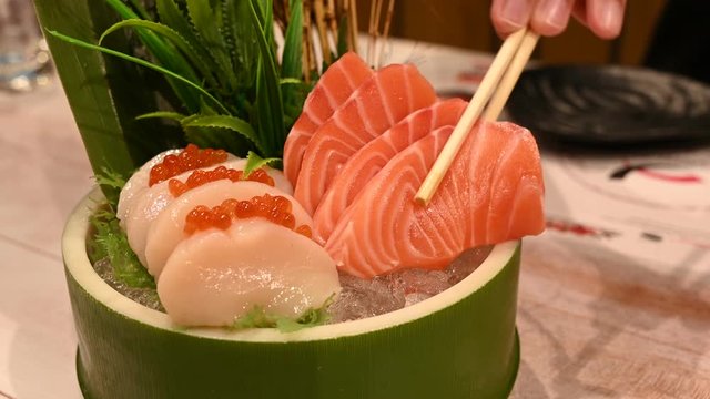 4K Asian woman eating salmon sashimi in japanese restaurant, young female holding chopsticks and eating salmon and hotate sashimi in lunch time. Lifestyle women eating traditional food concept.