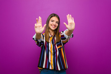young pretty woman smiling and looking friendly, showing number nine or ninth with hand forward,...