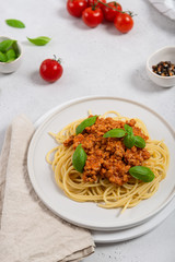 Spaghetti bolognese with basil garnish on white plate on white background.