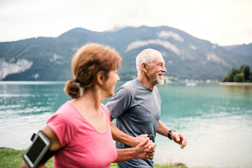 Fototapeta premium Senior pensioner couple with smartphone running by lake in nature.