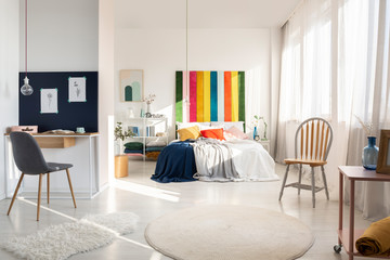 White bedroom interior with workspace with chair and rainbow colored bedhead