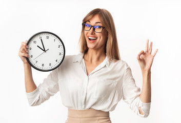 Happy Businesswoman Holding Clock Gesturing OK Standing On White Background