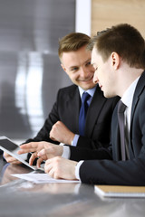 Businessman using tablet computer and work together with his colleague or partner at the glass desk in modern office. Unknown business people at meeting. Teamwork and partnership concept