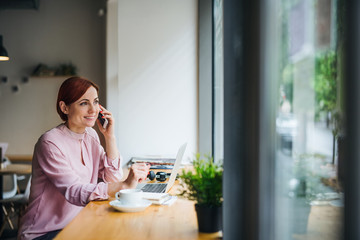 A woman with coffee and telephone sitting at the table in a cafe, making a phone call.