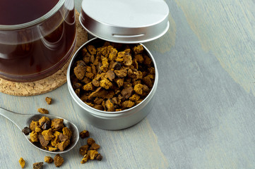 Natural and wild chaga mushroom pieces in container. Accompanied by a cup of hot chaga tea on gray wood background.