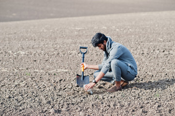 South asian agronomist farmer with shovel inspecting black soil. Agriculture production concept.