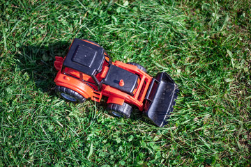 A tractor stands on the grass. Toy tractor on a green lawn. A toy for a child. Farming in miniature.