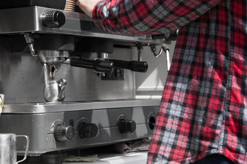 Bartender in a crippled shirt is making coffee on a machine.