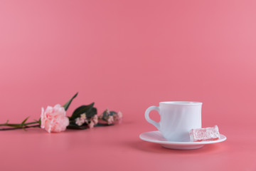 Fototapeta na wymiar A white cup of tea with a piece of lokum, turkish delight on the side, with delicate flowers on a pink background. Afternoon tea concept