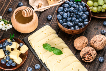 cheese, blueberries, grapes and honey on a wooden background