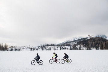 Side view of group of mountain bikers riding outdoors in winter.