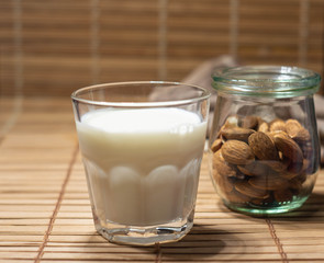 Almond milk poured in glass with almond nuts in glass jar