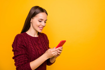 Naklejka premium Turned photo of charming lady holding her gadget looking at screen wearing burgundy jumper isolated over yellow background