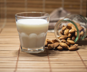 Almond milk poured in glass with almond nuts in glass jar