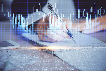 A woman hands writing information about stock market in notepad. Forex chart holograms in front....