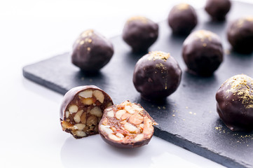 Handmade chocolates with peanuts and honey. Gourmet chocolates on a white background on the black ceramic board. Close-up. Soft focus
