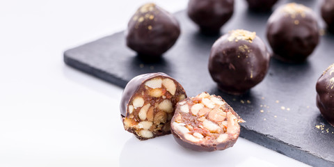 Food banner: Handmade chocolates with peanuts and honey. Gourmet chocolates on a white background on the black ceramic board. Close-up. Soft focus