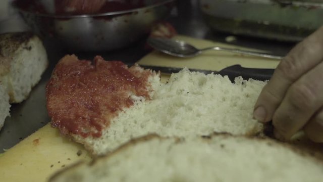 putting tomato sauce ( kunserva ) on to the traditional Maltese bread . Close up slow motion shot