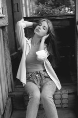 Beautiful young woman with long hair sitting on the porch. Black and white
