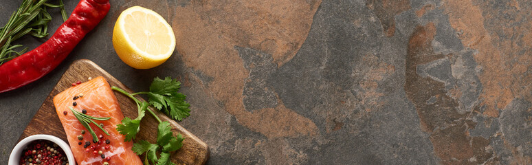 top view of raw salmon with peppercorns, parsley on wooden cutting board near lemon and chili pepper, panoramic shot