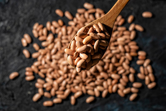 Overhead view of Phaseolus vulgaris, also called beans, chingadilla, grain, pocha, faba, caraota or bean brown with wooden spoon on dark background