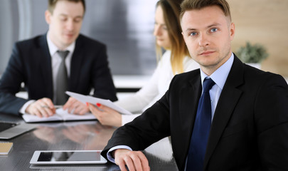 Fototapeta premium Businessman headshot at meeting in modern office. Unknown entrepreneur sitting with colleagues at the background. Teamwork and partnership concept