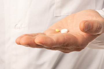 The doctor in white clothes, and blue gloves, with a stethoscope on his neck, holds out pills. Close up