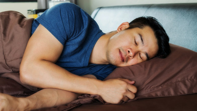 Asian young man sleeps on a brown bed.