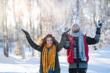 Portrait of couple standing outdoors in snow in winter forest, throwing snow.