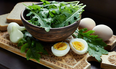 Rucola or rocket salad with boiled egg, green onion, bread and sour cream as simple country food on rustic wooden cutting board, closeup, copy space, vegetarian food concept