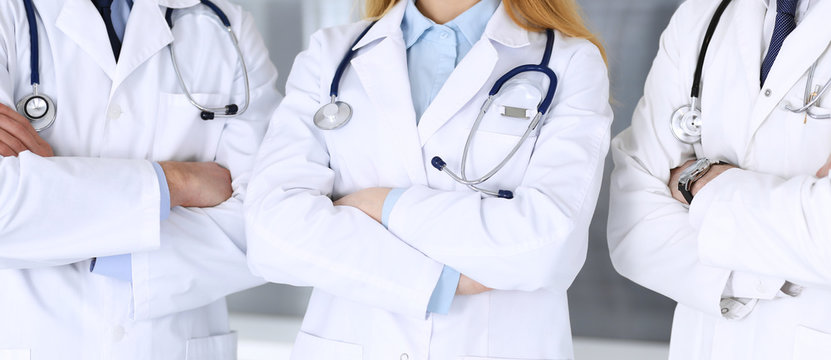 Group of modern doctors standing as a team with arms crossed in hospital office, close-up. Physicians ready to examine and help patients. Medical help, insurance in health care, best treatment and