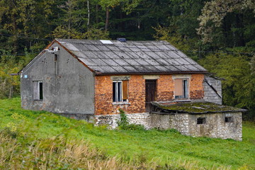 an old ramshackle red brick house by the woods, without glass or trim, with a ruined roof....