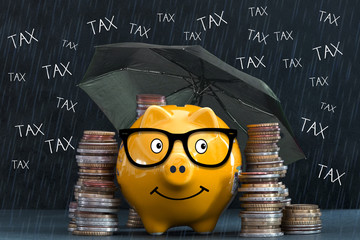 Yellow piggy bank with piles of money protected by the umbrella against taxes