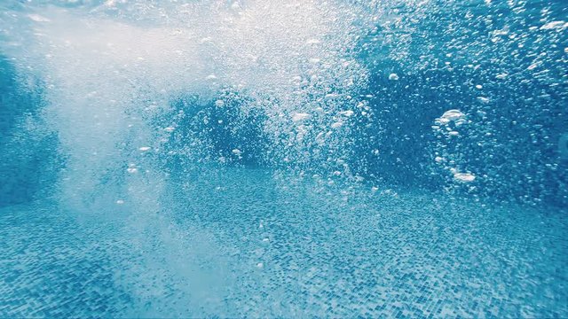 Slow motion of sir bubbles in a pool from water jet, underwater view