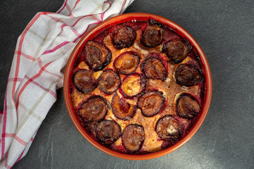 Original plum torte NYT's recipe. Homemade pie with halves of fresh plums in ceramic shape.