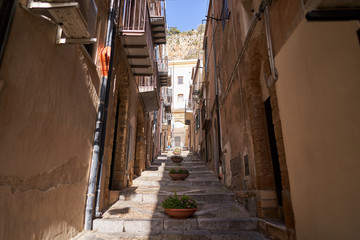 Fototapeta na wymiar Typical example of historic mediterranean architecture of italian narrow small street in city Cefalu on the island Sicily, houses build from stones with balcony. Picture is taken in sunny spring day.
