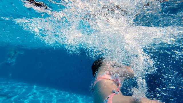 Cute girl jumping into the pool and trying to swim underwater