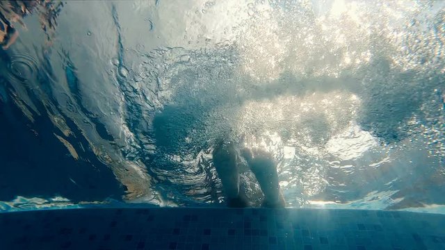 Slow motion of legs swinging and making air bubbles underwater in a pool