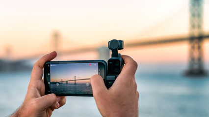 A photographer is using DJI Osmo Pocket to take footage of a Bay Bridge, San Francisco, USA