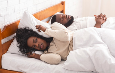 Black woman suffering from snoring boyfriend, closing ears with pillow.