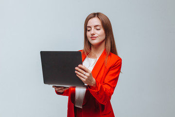 girl in a red jacket holds a laptop on a light background