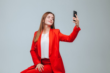 Naklejka premium girl in a red jacket takes a selfie on the phone on a gray background