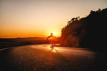 Fototapeta na wymiar Skater descending a road at sunset