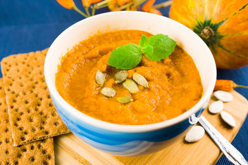 Pumpkin soup in a bowl is served with herbs, pumpkin seeds and rye bread. Vegan soup. Blue background.