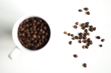 Coffee beans are sprinkled on the table next to a cup of coffee beans.