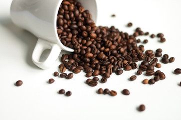 Roasted coffee sprinkled from a white bowl on a white background