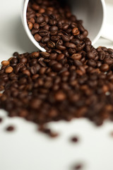 Coffee is beautifully sprinkled from a white bowl on a white background. Vertical frame with a blurred background.