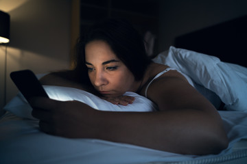 Young woman or girl using smartphone app social media while lying in bed at night